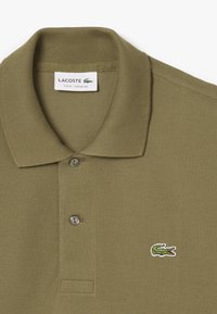 Klasyczna polo w oliwkowym kolorze, z ribbowanym kołnierzykiem, zapinana na dwa guziki oraz z wyszywaną logo krokodyla na piersi.