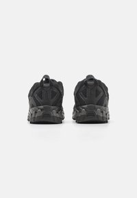 Schwarze Sportschuhe mit einem strukturierten Netz-Obermaterial und verstärktem Fersenbereich. Wuchtige Gummisohle mit ausgeprägten Traktionsmustern.