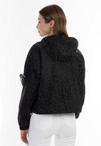 Giacca nera con cappuccio, caratterizzata da un motivo geometrico testurizzato, polsi elasticizzati e una tasca con zip sulla manica sinistra.