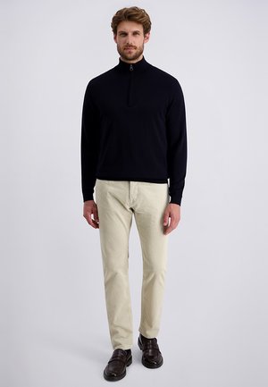 Marineblauer Reißverschluss-Pullover mit langen Ärmeln und glatter Textur; kombiniert mit hellbeigen Cordhose mit flacher Vorderseite und braunen Slippern.