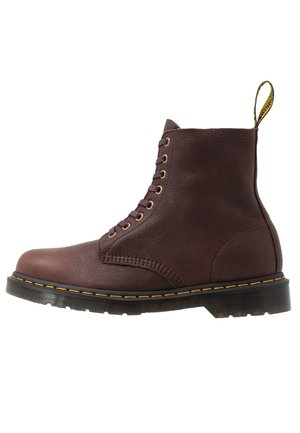 Brązowy skórzany botek na sznurowadła z żółtym przeszyciem, czarną podeszwą i pętelką z tyłu, widoczny z boku na białym tle.