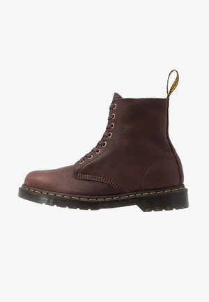 Botte en cuir marron à lacets avec surpiqûres jaunes, semelle noire et languette à l'arrière, vue de profil sur fond blanc.