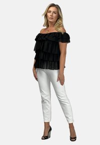 Czarny top bez ramiączek z warstwowymi falbanami, w połączeniu z białymi dopasowanymi spodniami. Modelka nosząca czarne szpilki z teksturowanymi akcentami.