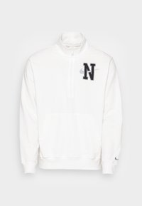 Sudadera blanca de medio cierre con un bolsillo frontal, que presenta un parche negro con la 'N' y el logo gris de Nike en el pecho. Tejido suave y puños acanalados.