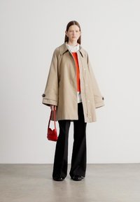 Bézs színű, nagy galléros, bő szabású kabát, alatta piros pulóver, fekete nadrág és egy kis piros kézitáska. Sima anyag minimális díszítéssel.