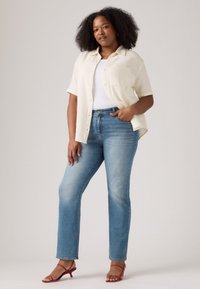 Lettvekts kremfarget kortermet skjorte med knapper, hvit singlet, blå rette jeans og røde hælsandaler med stropper.
