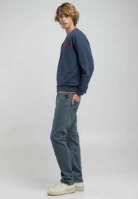 Felpa blu navy a girocollo con un piccolo logo rosso, abbinata a jeans azzurri e sneakers bianche, caratterizzata da una vestibilità comoda.