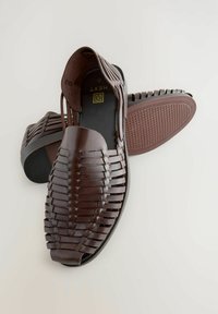 Sandalias de cuero marrón con un patrón trenzado, punta abierta, tacón bajo y suela de goma texturizada. Presentan una plantilla suave y una plantilla con marca.