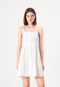 Λευκό φόρεμα με ρυθμιζόμενες τιράντες, κουμπί μπροστά και δαντέλα στη μέση. Φούστα με φλαιρ και συγκεντρωμένες τάξεις; ελαφρύ ύφασμα.