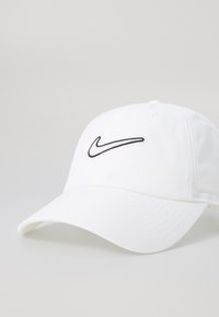 Hvid baseballkasket med en let buet skygge, prydet med et sort broderet Nike Swoosh foran. Lavet af struktureret stof.