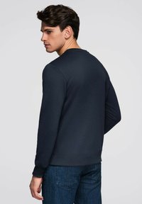 Felpa blu marina in tessuto morbido, con scollo rotondo e polsini a coste. Caratterizzata da una vestibilità rilassata e dettagli minimalisti.