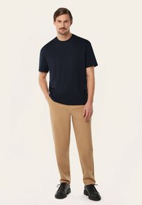 Marineblauwe t-shirt met korte mouwen gecombineerd met beige broeken; beide zijn slim fit, met een gestructureerde stof. De outfit wordt aangevuld met zwarte veterschoenen.