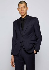 Marynarski garnitur skrojony na miarę z jednorzędową marynarką, klapami w kształcie notcha i dwoma przednimi kieszeniami. W połączeniu z czarnym krawatem i koszulą wizytową.