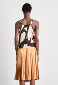 Débardeur noir avec des motifs abstraits orange, doté de bretelles à pois ; associé à une jupe plissée dorée arrivant au genou.