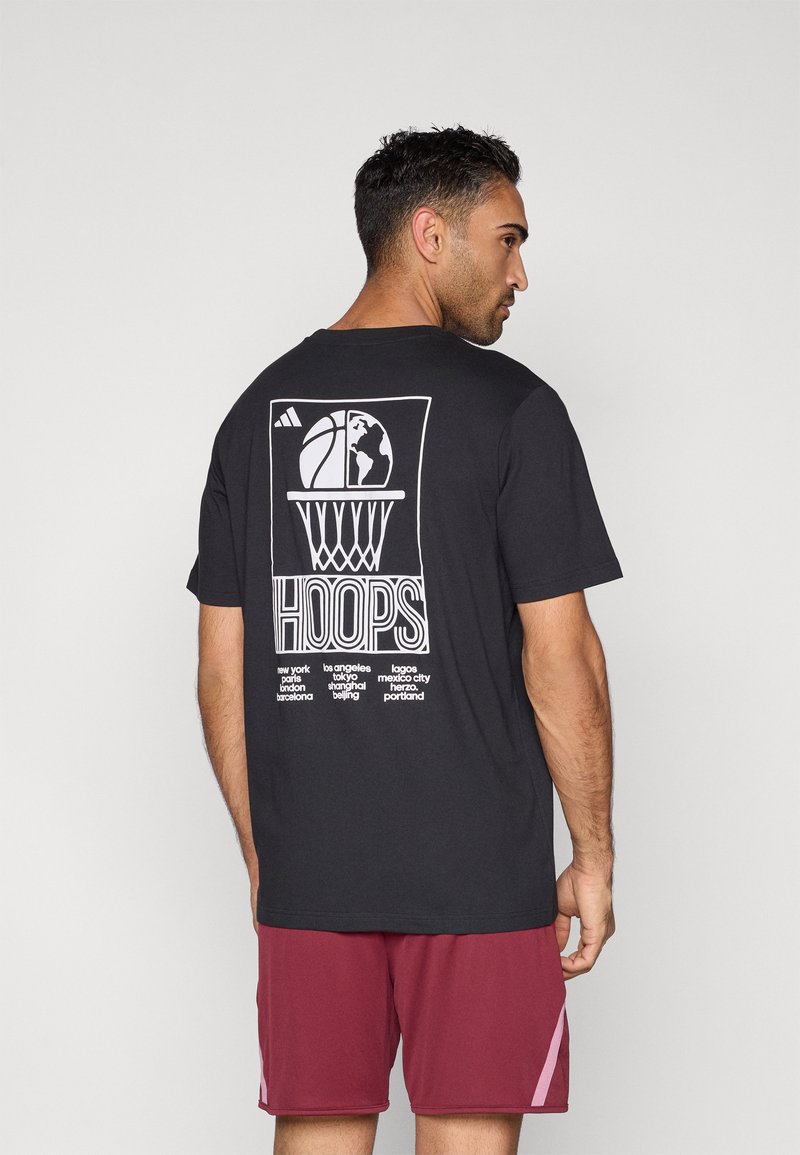 Zwart katoenen T-shirt met een wit grafisch ontwerp van een basketbal, wereldbol en de tekst "HOOPS" op de achterkant; model draagt bordeauxrode shorts.