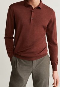 Polo a maniche lunghe bordeaux con colletto a tre bottoni, texture morbida e polsini a coste, abbinato a pantaloni grigi a quadri.