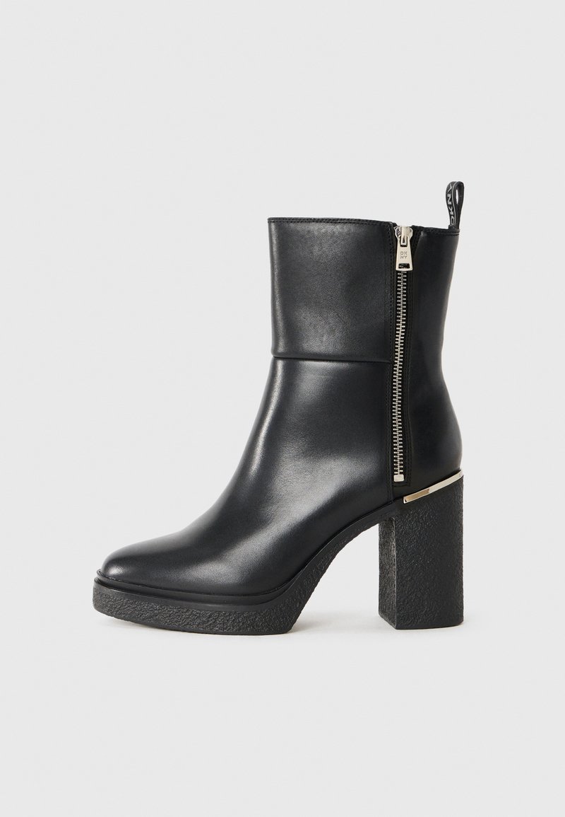 Bottine noire en cuir lisse, avec une fermeture éclair sur le côté et un talon bloc texturé. Conception facile à enfiler avec un bout arrondi.