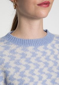 Maglione a motivo coda di pavone in blu chiaro e crema, con scollatura rotonda, texture a maglia e dettaglio del colletto a coste.