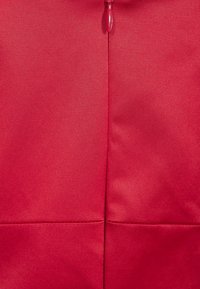 Rode stof met een gladde textuur, met een verticale naad en een kleine ritssluiting bovenaan. Eenvoudig, effen ontwerp zonder patronen.