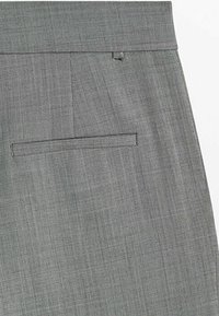 Section de pantalon de costume gris sur mesure montrant la taille, la boucle de ceinture, et une poche arrière passepoilée avec une fine texture diagonale du tissu.