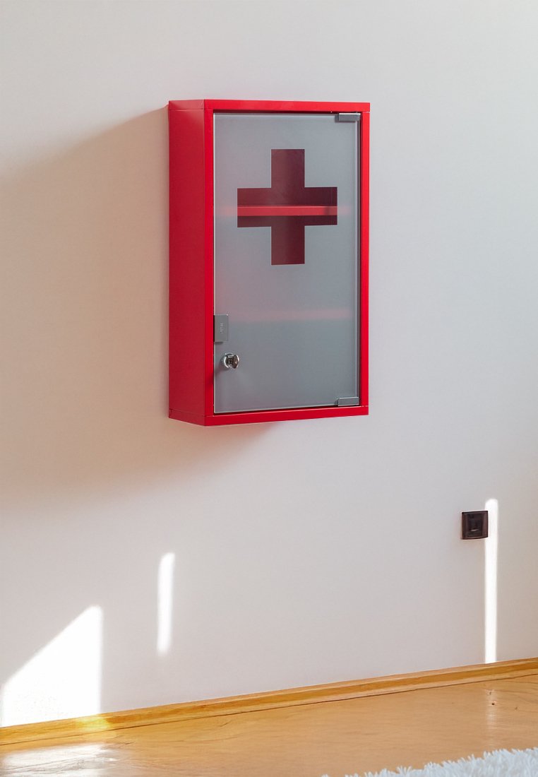 Roter Medizinschrank mit einer Glasfront, versehen mit einem großen roten Kreuz. Glatte Textur, rechteckige Form und ein Schlüsselloch auf der linken Seite.