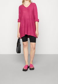 Rosa stickad tunika med V-ringning och trekvartsärmar, kombinerad med svarta cykelshorts och rosa slidesandaler. Svart handväska ingår.