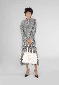 Borsa a mano in pelle bianca con dettaglio intrecciato e chiusura a fibbia, abbinata a un outfit con motivo bianco e nero, composto da una camicia con bottoni e pantaloni a gamba larga.