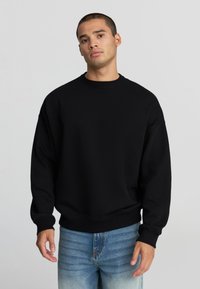 Felpa nera, colletto rotondo, vestibilità comoda, realizzata in tessuto morbido. Polsini e orlo a costine, abbinata a jeans azzurri chiari. Design semplice, senza motivi.