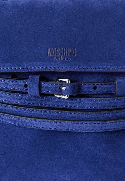 Borsa in suede blu con dettaglio simile a una cintura, hardware argentato e branding impresso. Texture liscia con accenti cuciti.