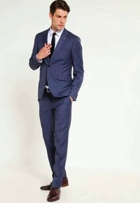 Marineblå dress med skreddersydd passform, ensidig knappeslag, klaffeslag, og bukser med flat fron, kombinert med en hvit skjorte og svart slips.