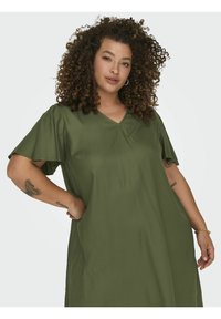 Alyvuogių žalia, trumpomis rankovėmis suknelė su v-kaklu. Lycra tekstūra ir laisvas kirpimas, puošti dekoratyvine siūlė ir kontrastingomis rankovėmis.