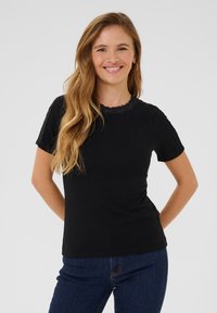 T-shirt noir à manches courtes avec un col en dentelle festonné, fabriqué en tissu côtelé. Porté avec un jean bleu, présentant une silhouette ajustée.