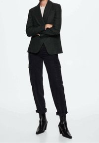Donkergroene op maat gemaakte blazer over een lichte top, gecombineerd met zwarte cargo broeken met zijzakken en opgerolde boorden, aangevuld met hakken.