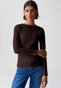 Brown ribbed long-sleeve top with a boat neckline, featuring textured fabric and fitted design, paired with blue straight-leg jeans.
