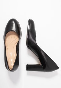 Chaussures à talons hauts noires avec une finition en cuir lisse, bout arrondi et talon épais ; dotées d'une semelle intérieure rembourrée pour le confort.