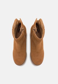 Botas de tobillo de ante marrón con una textura suave, cremalleras laterales y un forro suave. El diseño presenta una puntera redondeada y costuras mínimas.