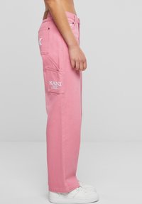 Pantalones cargo rosas con un diseño de pierna recta, que cuentan con bolsillos en la parte frontal, un parche con logo y detalles de costura blanca. Hechos de tela de algodón.