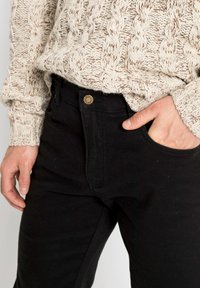 Pantaloni in cotone neri con design a cinque tasche, dotati di chiusura con bottone metallico e una texture liscia, abbinati a un maglione in maglia crema.