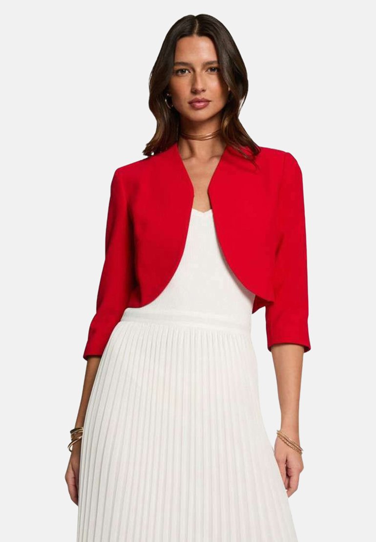 Veste rouge courte en tissu lisse avec un col arrondi et des manches trois-quarts, associée à une robe plissée blanche.