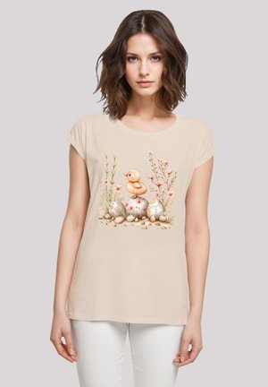 Hellbeige T-Shirt mit kurzen Ärmeln, mit einer Illustration eines Entenbabys und dekorierten Eiern in Pastellfarben, umgeben von floralen Details.