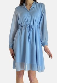 Robe bleu clair, longueur genou, avec de longues manches transparentes, un devant à boutons et une taille à cordon pour un ajustement réglable. Tissu lisse et léger.
