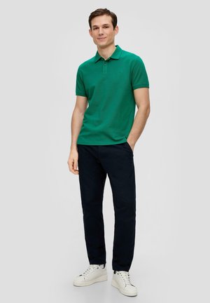 Groene polo met korte mouwen, gecombineerd met een marineblauwe broek en witte sneakers. Zachte textuur en een klassiek kraagontwerp.