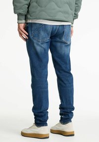 Jeans in denim blu scuro con gamba affusolata, caratterizzati da tasche posteriori e leggera scoloritura, abbinati a sneaker di colore crema.