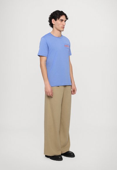 T-shirt en coton bleu clair à manches courtes avec un motif sur la poitrine. Associé à un pantalon large beige et des bottes noires. Design simple.