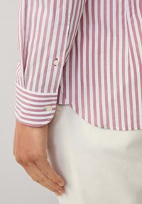 Pruhovaná košile s růžovými a bílými vertikálními pruhy. Obsahuje knoflík na manžetě s malým kulatým knoflíkem. Hladká tkanina s jemnou strukturou.