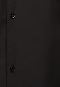 Μαύρο ύφασμα με δύο μαύρα στρογγυλά κουμπιά ραμμένα κατά μήκος μιας κάθετης ραφής.