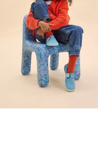 Barns blå textilsandaler med rem framtill, bärs tillsammans med orange strumpor, sittandes på en blå prickig plaststol.