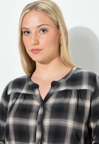 Czarna i biała bluzka w kratkę z okrągłym dekoltem, zapięciem na guziki oraz fałdami z przodu. Miękki materiał o teksturowanym wykończeniu.