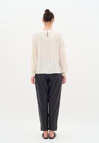 Blusa avorio chiaro con maniche lunghe elastiche e dettaglio a chiave nella parte posteriore, abbinata a pantaloni in pelle nera dal fit morbido.