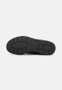Semelle de chaussure en caoutchouc noir avec de profonds canaux, motifs texturés et logo en relief. Présente un design robuste pour l'adhérence et la durabilité.